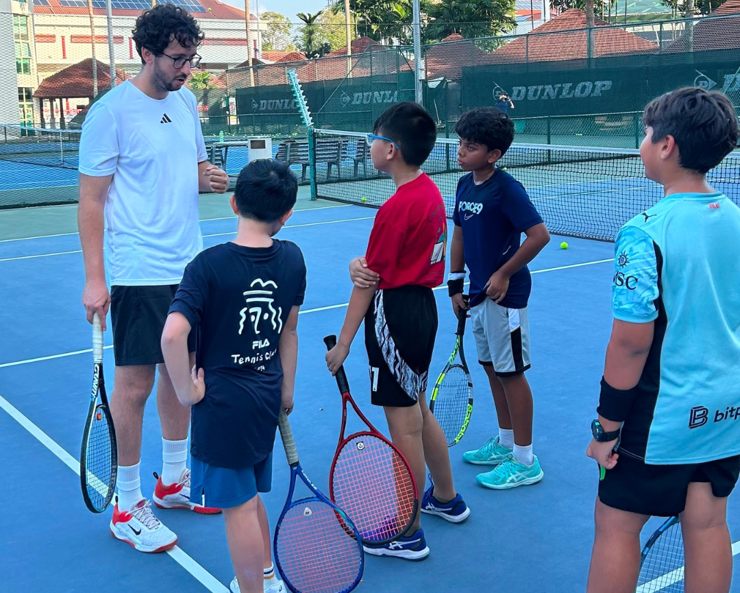 RB Tennis Academy Super Smashers Junior Groups featuring a group of children and an adult on a blue tennis court under a clear sky